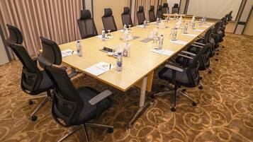 Un salón de conferencias con una larga mesa, sillas negras, botellas de agua y pañuelos.
