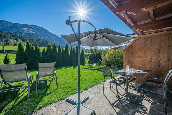 Une terrasse extérieure avec une table et des chaises, un grand parasol et une vue sur une montagne.
