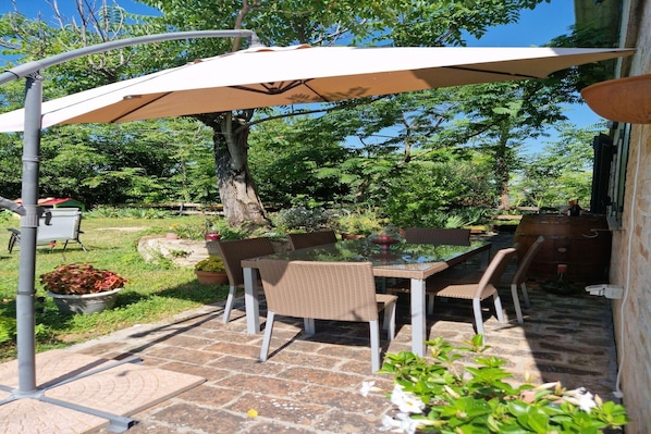 An outdoor patio with a glass table, wicker chairs, and a large umbrella.