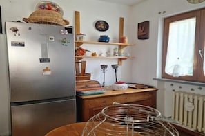 Une cuisine équipée d’un réfrigérateur, d’étagères en bois, d’une fenêtre et d’un radiateur.