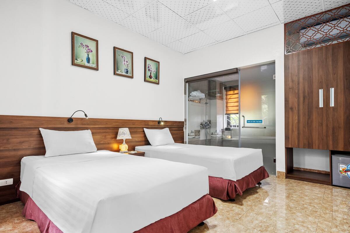 A hotel room with two beds, a bathroom with a glass shower, and a minibar.