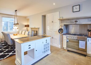 A modern kitchen with a central island, white cabinetry, a built-in stove, and a dining area with a black and white rug. - Penhill House (Leyburn)