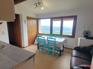 Eine Küche mit Esstisch und Stühlen, ein schwarzes Ledersofa, ein Fenster mit Landschaftsblick und einer Deckenleuchte.