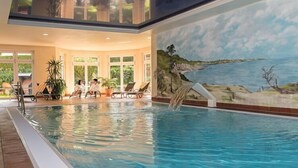 An indoor swimming pool with clear blue water, surrounded by lounge chairs and potted plants.