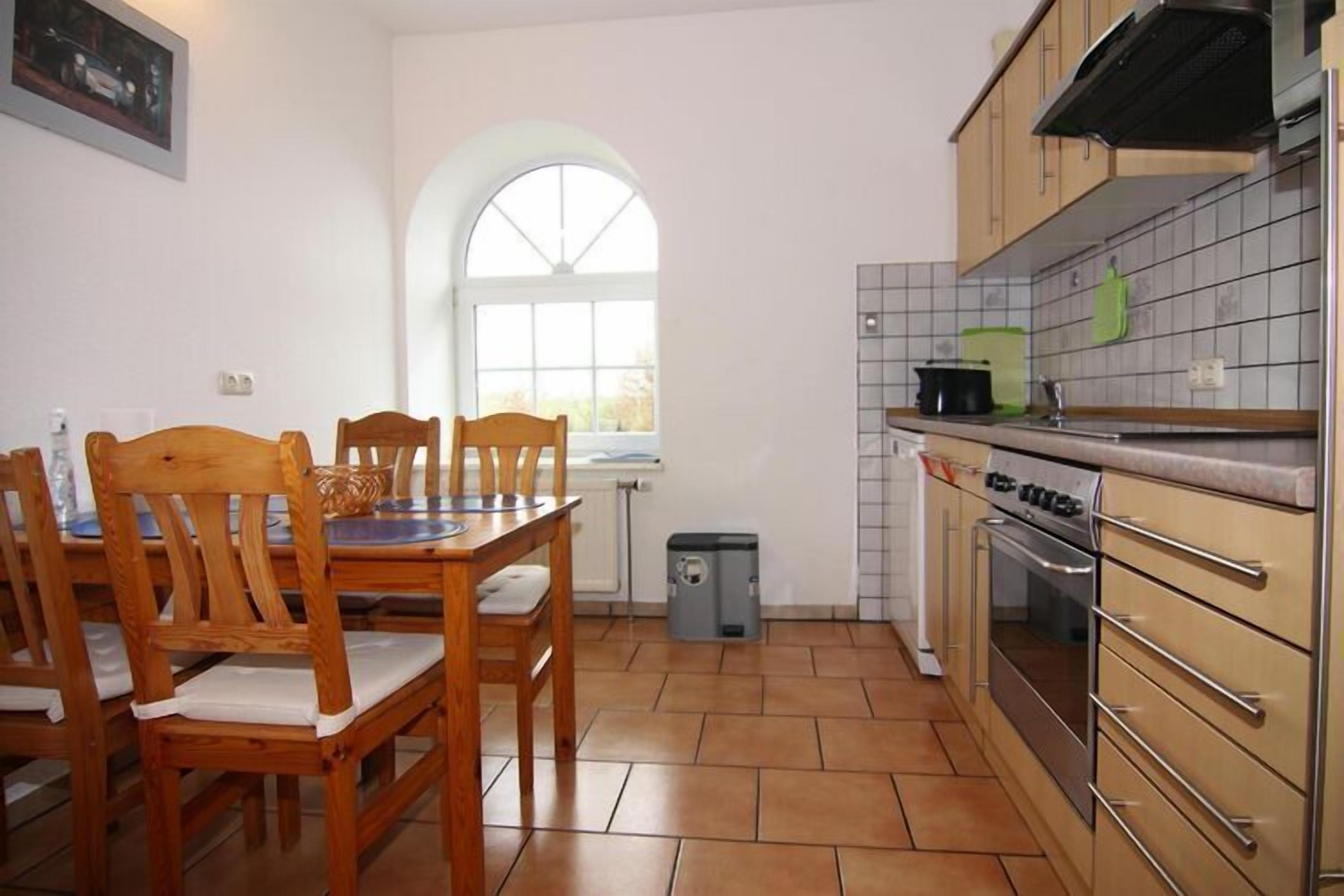 A kitchen with wooden chairs, a dining table, a window, a stove, and cabinets.