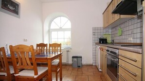A kitchen with wooden chairs, a dining table, a window, a stove, and cabinets. - Ferienwohnanlage Gut Bundhorst, Stolpe (Stolpe)