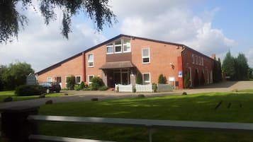 Un bâtiment en briques de deux étages, doté d’une entrée centrale, d’une allée bordée d’une clôture et d’un panneau indiquant un espace de stationnement.