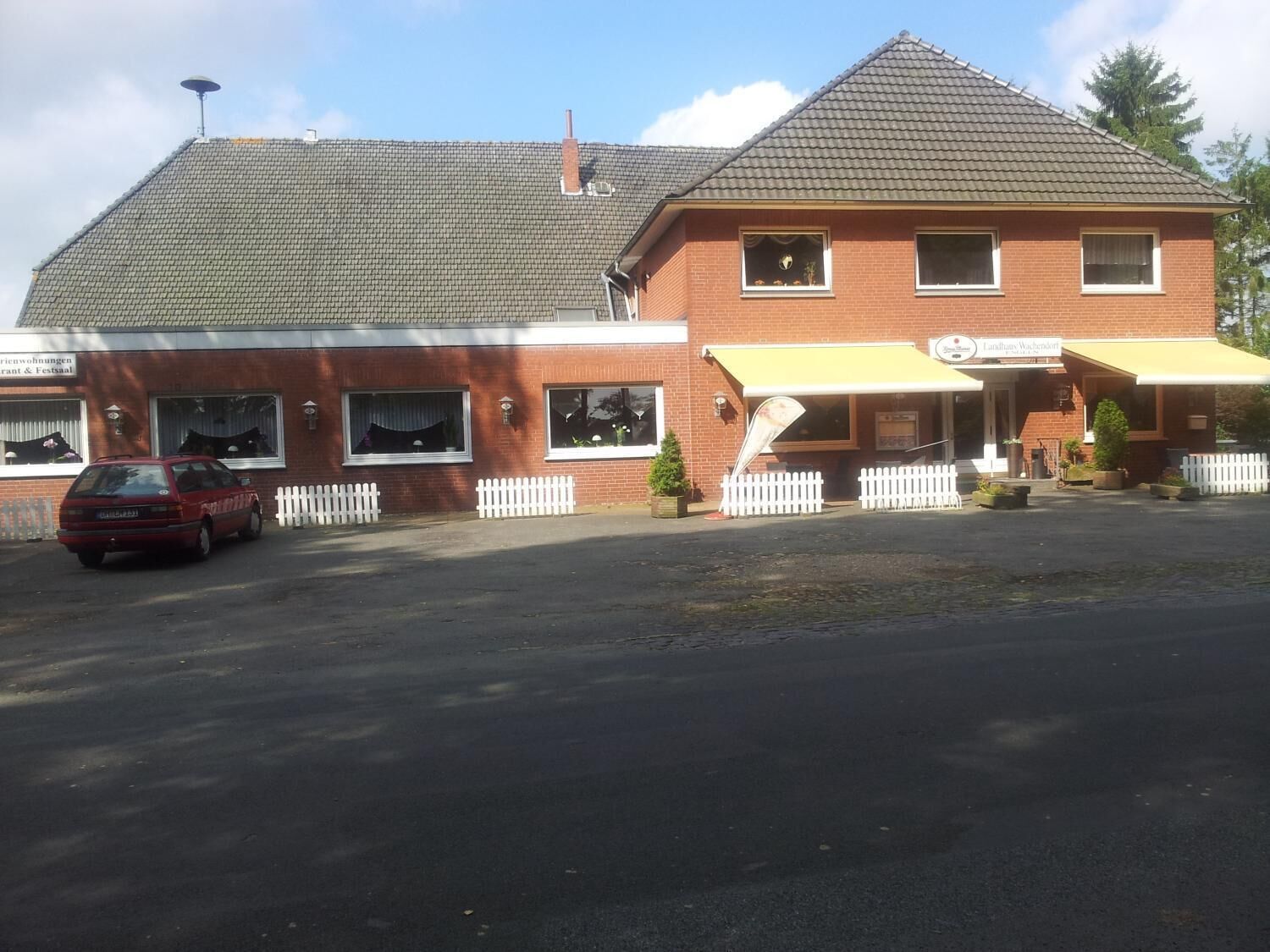 Un bâtiment à deux étages, doté d’un toit plat, avec une voiture garée devant et une clôture blanche en piquets.