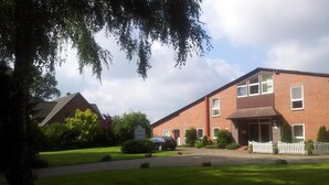 A two-story brick building with a white picket fence, a paved driveway, and a well-maintained lawn. - Hotel Landhaus Wachendorf (Bruchhausen-Vilsen)