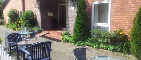 An outdoor seating area with tables and chairs, a brick building, and a white picket fence.