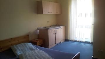 Una habitación pequeña y sencilla con cama, una kitchenette pequeña y una ventana con cortinas.