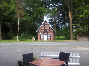 A small, traditional building with a white door and windows, surrounded by trees. In front of the building, there is a paved area with two chairs and a table. - Hotel Landhaus Wachendorf (Bruchhausen-Vilsen)