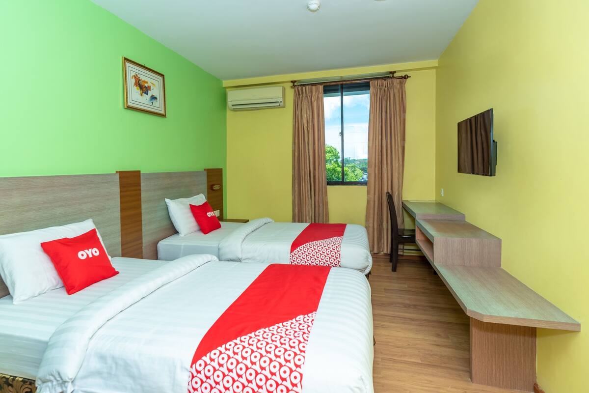 A hotel room with two beds, a desk, and a window with curtains.