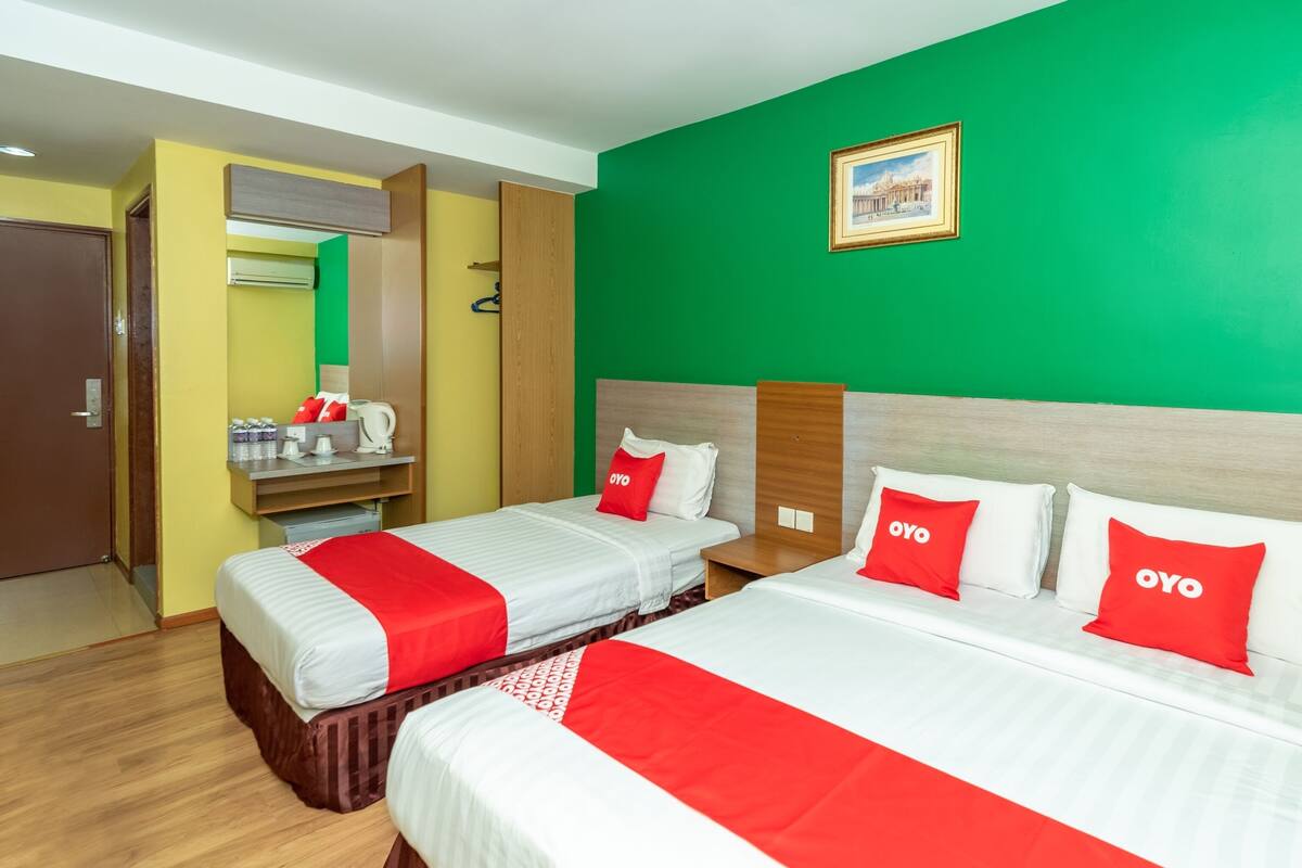 A hotel room with two beds, each with red and white bedding and pillows, a green wall, and a framed picture above the beds.
