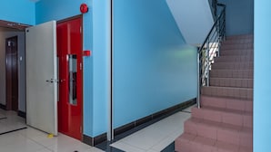 A hallway with a red door, a staircase, and a blue wall. - Capital O 89538 Ocean Hotel (Labuan)