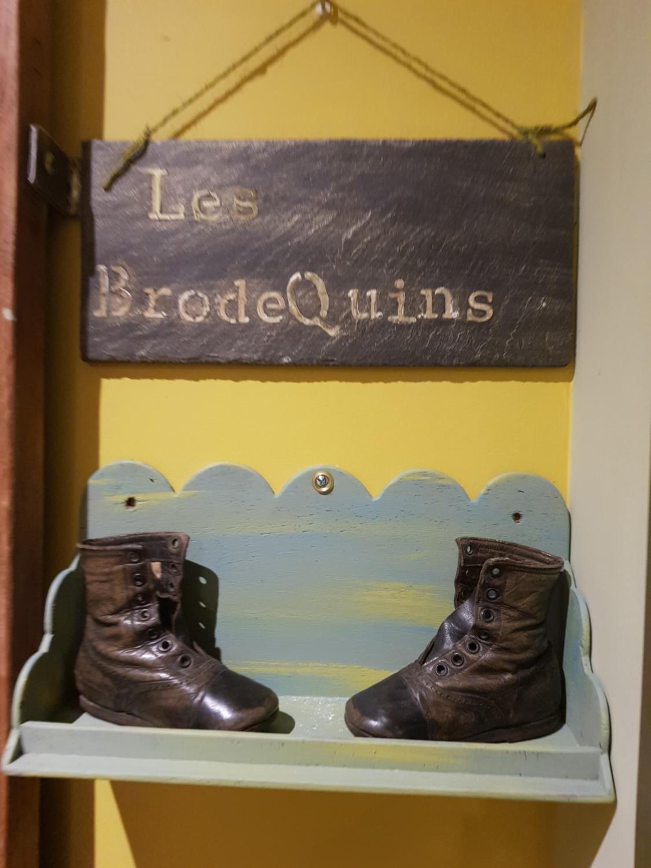 Une enseigne avec l’inscription « Les BrodeQuins » et une paire de bottes posées sur une étagère.