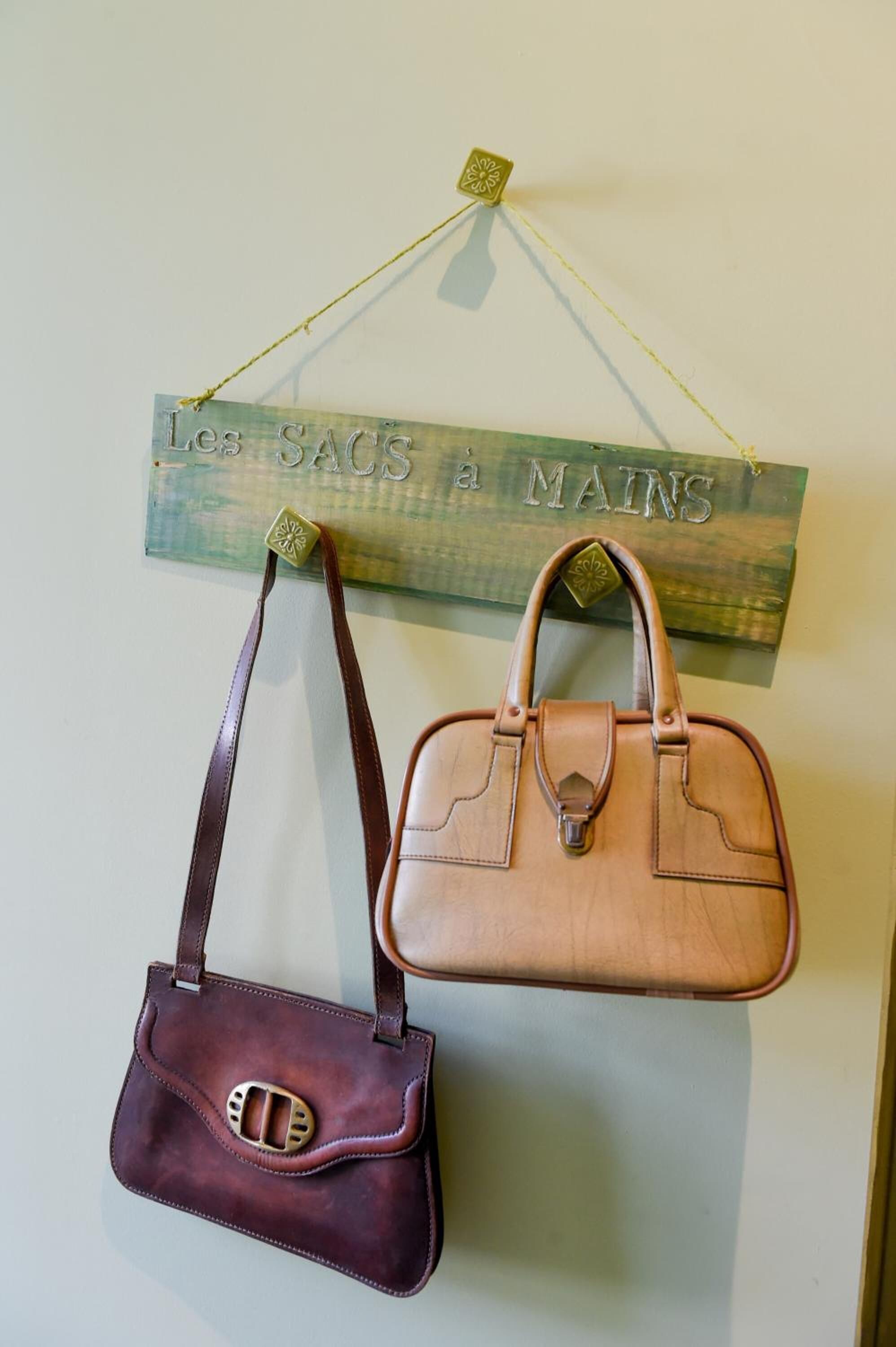 Two handbags hanging from a wooden sign with the text "Les Sacs a Mains".