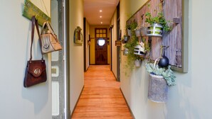 A hallway with wooden flooring, a wooden door at the end, and a wall with hanging plants and a sign. - l'En Vert (Bagnères-de-Bigorre)