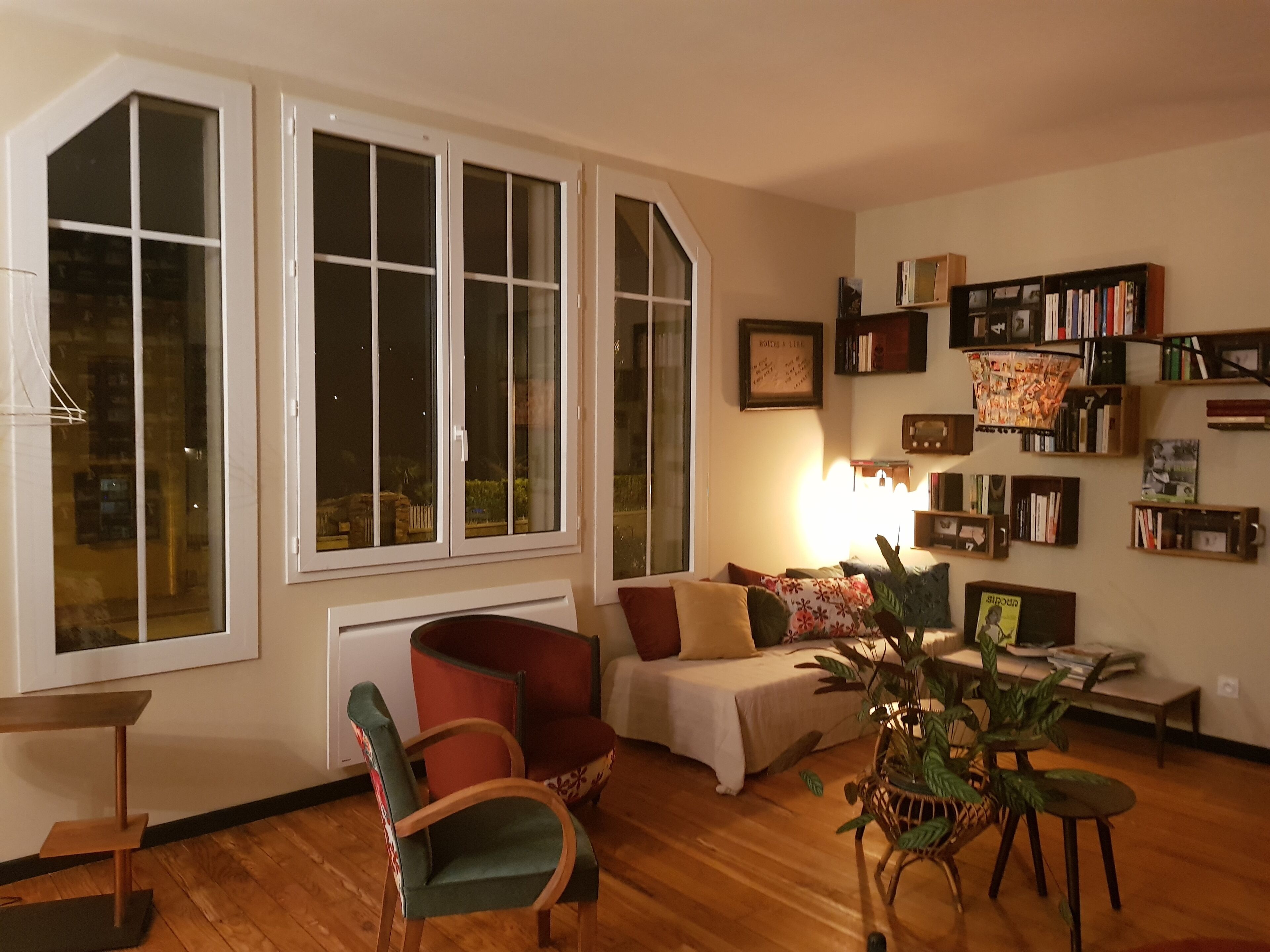 A cozy living room with a large window, a bookshelf, and a comfortable seating area.