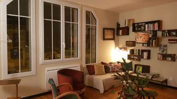 A cozy living room with a large window, a bookshelf, and a comfortable seating area.