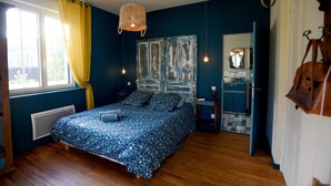A bedroom with a bed, a bedside table, a hanging light, a window with curtains, and a door leading to a bathroom. - l'En Vert (Bagnères-de-Bigorre)