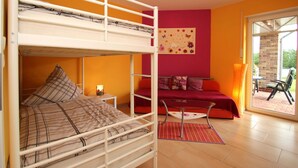 Ein Zimmer mit einem Etagenbett, einem roten Schlafsofa und einer Glastür zu einem Außenbereich.