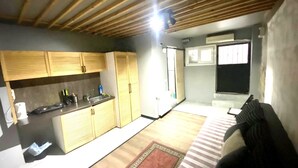 A compact kitchen with wooden cabinets, a sink, and a small countertop. There is a window with bars, a door, and a patterned rug on the floor. - Mara Suite Taxim (Istanbul)