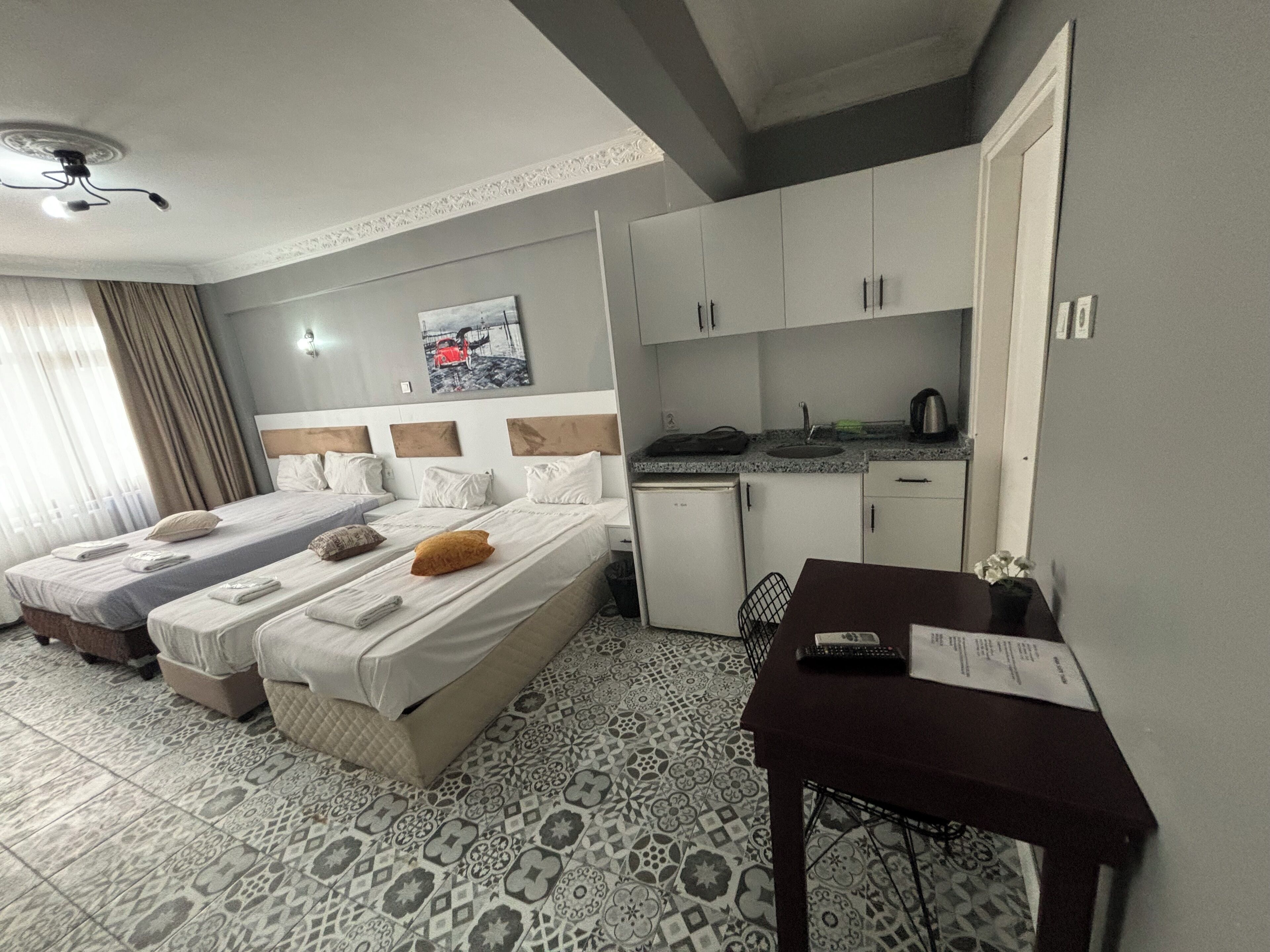 A hotel room with two beds, a small kitchenette, and a desk with a chair.
