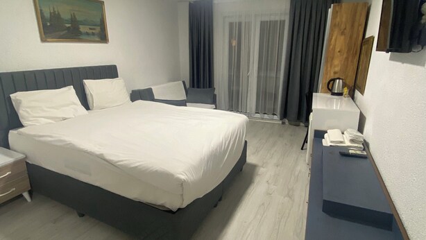 A modern hotel room with a large bed, a bedside table, a desk, a chair, a painting on the wall, and a window with curtains. - Mara Suite Taxim (Istanbul)
