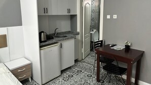A compact kitchen with white cabinets, a sink, and a small refrigerator. There's a dining table with chairs and a patterned floor. - Mara Suite Taxim (Istanbul)