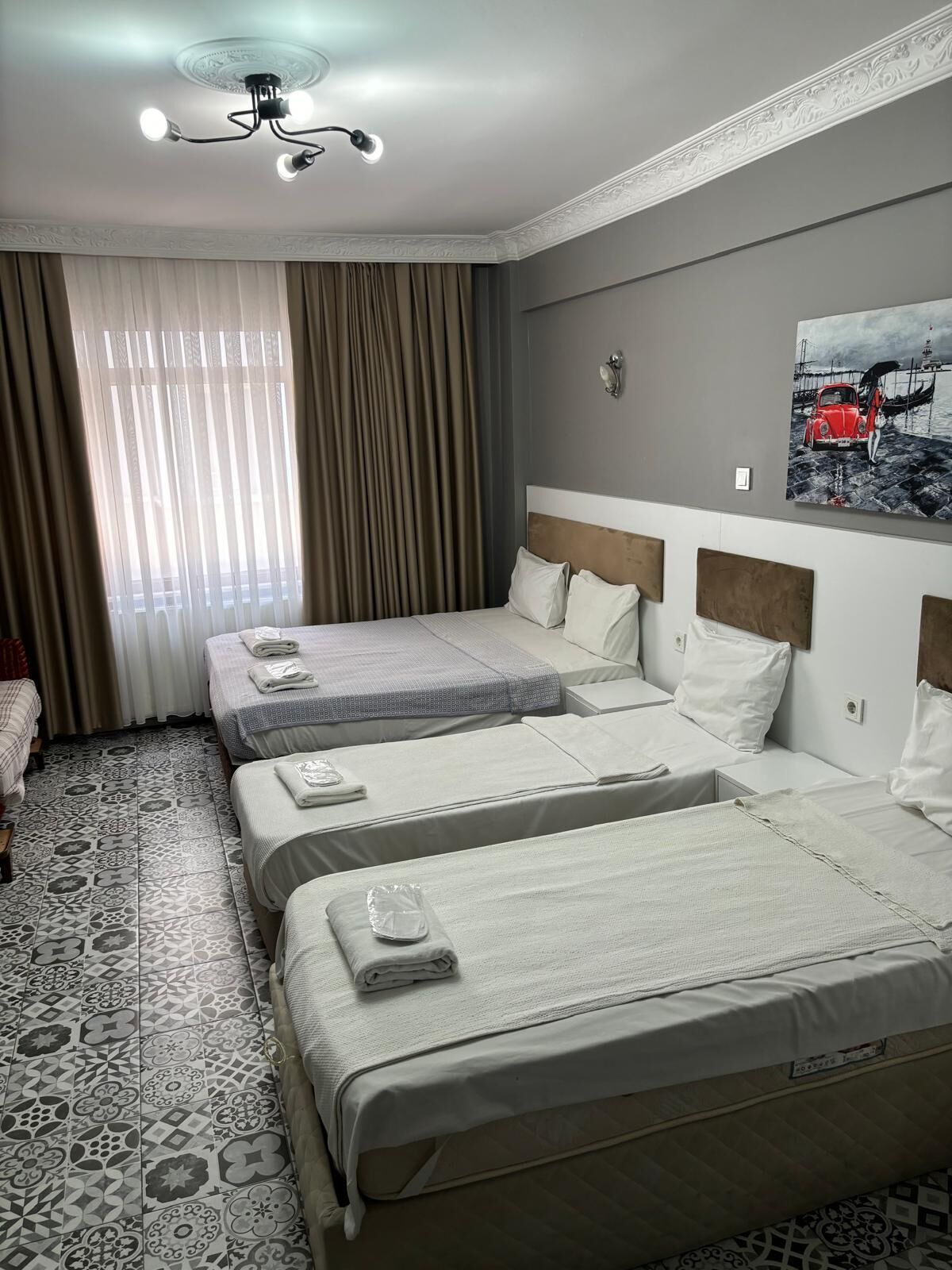 A hotel room with two beds, a ceiling fan, a painting, and patterned floor tiles.