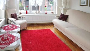 A living room with a red rug, white furniture, a window with curtains, and a vase with flowers. - Holiday Home in Misdroy near Baltic Sea (Miedzyzdroje)