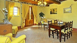 A dining area with a wooden table and chairs, yellow curtains, and a chandelier. - Estate in Monte Serra with Pool & Olive Trees (Pisa)