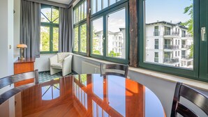 A dining area with a round table, chairs, and a view of buildings through large windows. - SEETELHOTEL Villa Waldesruh (Heringsdorf)