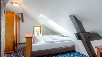 Ein Schlafzimmer mit schrägen Wänden, einem Bett mit weißer Bettwäsche, einem Holzschrank und einem gemusterten Teppich.