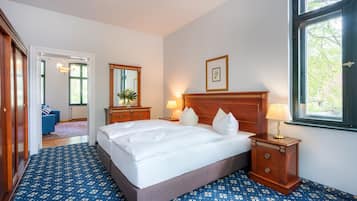 Habitación de hotel con una cama grande, una mesita de noche de madera con una lámpara, un cuadro en la pared y vistas al exterior a través de una ventana.