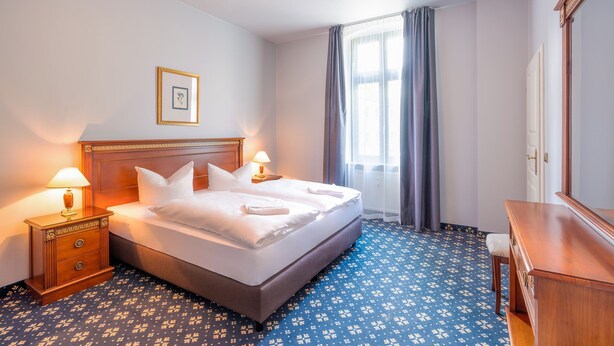 Una habitación de hotel con cama, mesita de noche, cómoda y ventana con cortinas.
