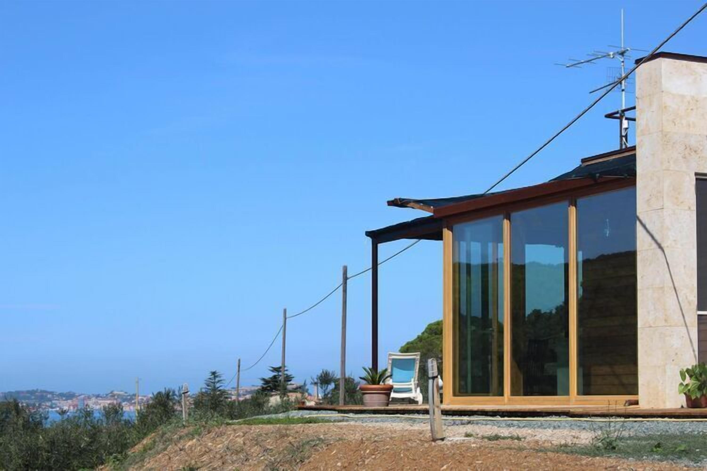 A modern house with large glass windows, a sloped roof, and a view of the sea.