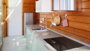A compact kitchen with wooden walls, a built-in stove, a sink, and a refrigerator.