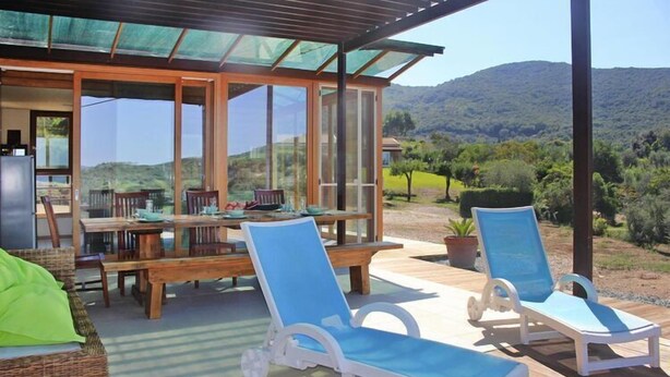 A covered outdoor seating area with a table and chairs, a sofa, and two sun loungers.