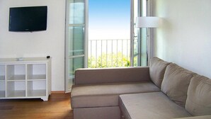 Una sala de estar con un sofá seccional color beige, un televisor de pantalla plana montado en la pared y un ventanal con vistas a zonas verdes.
