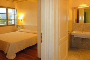 A bedroom with a bed, a bedside table, a nightstand, a window with a view, and a bathroom with a sink and mirror. - Apartment in Elba with Panoramic Views (Rio nell'Elba)