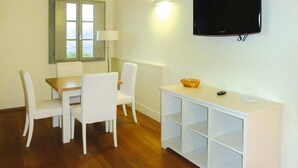 Una habitación con una mesa de comedor y sillas, un televisor montado en la pared y un armario blanco con estantes.