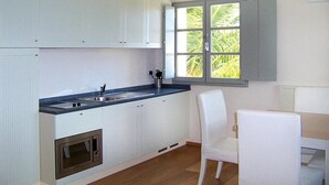 Una cocina moderna con armarios blancos, microondas integrado, pileta doble y ventana con vista a follaje.