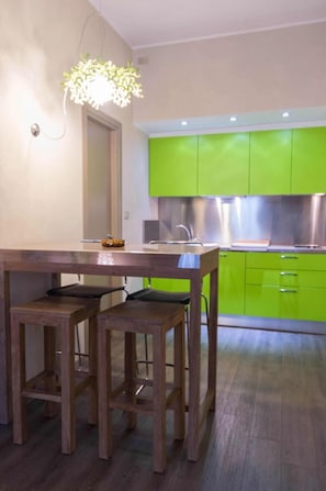 A modern kitchen with green cabinets, a wooden dining table with two chairs, and a pendant light.