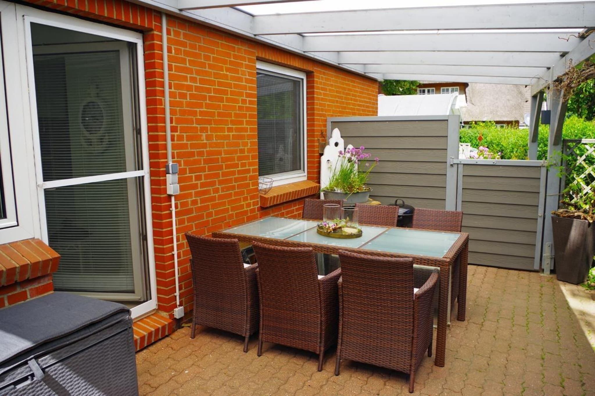 A patio with a glass-top table, wicker chairs, and a brick wall.