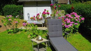 A garden with a lounge chair, a small table with a candle, and blooming flowers.