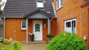 A brick house with a white door, a small porch, and a garden with flowers and bushes.