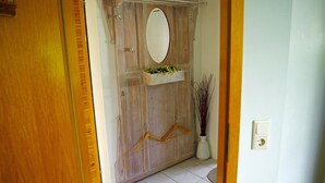 A wooden door with a mirror, a hanging plant, and a wall-mounted light switch.