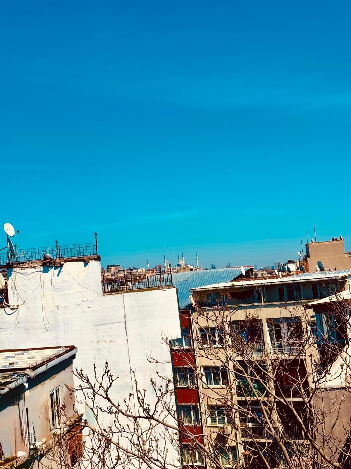 A high-rise building with multiple balconies, satellite dishes, and a clear blue sky.